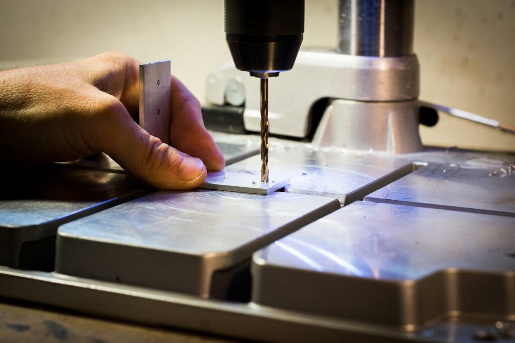 Person drilling a metal bar on a drilling machine, with the operator's hand visible