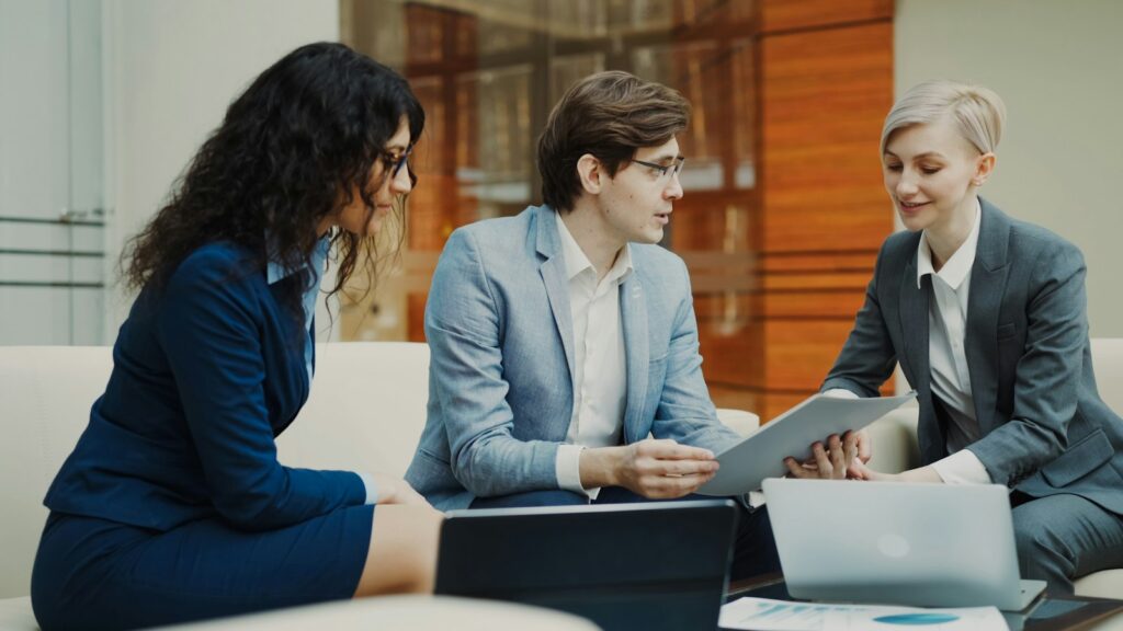 Three professionals sit at a table discussing documents, as in preparing a regulatory application