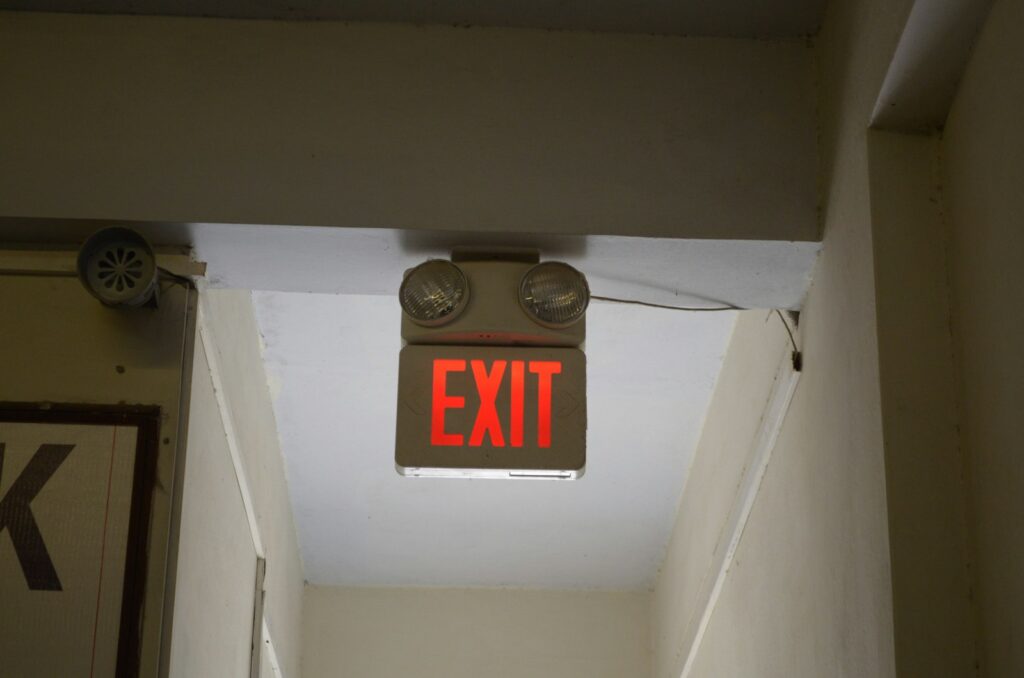 Red exit sign hanging from the ceiling of a hallway, marking the escape route