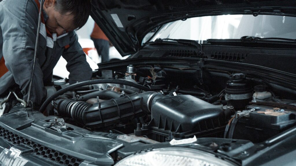 Mechanic in a grey uniform inspecting the engine of a car